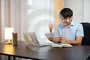 Asian handsome man reading acceptance letter for job application who pass the qualifying exam with joy and success at their home