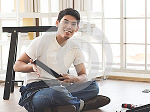 Asian  handsome young  man trying to assemble knock down furniture , smiling and looking at camera