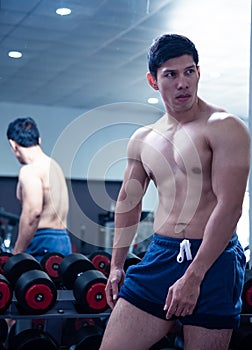 Asian handsome young muscular asian man exercising bodybuilder  in front of a glass in the gym .Guy flexing trains his bicep