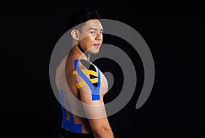 Asian handsome young muscular man getting pain and putting kinesiology tape on his body while standing on isolated black