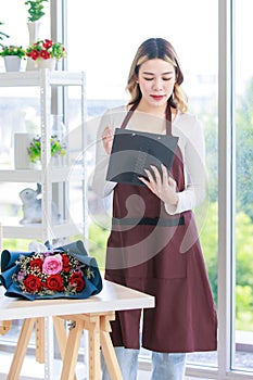 Asian happy cheerful female florist flower shop owner holding pink roses bouquet decorating in white ceramic vase for customer