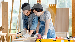 Asian happy cheerful male dad son carpenter woodworker colleague in jeans outfit with safety gloves helping using hand saw cutting