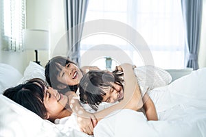 Asian happy children jumping on bed to waking up mother in the morning. Young little girl sibling daughters enjoy play with loving