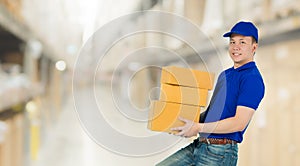 Asian happy delivery man wearing a blue shirt carrying paper parcel boxes isolated on blur interior warehouse in the shopping mall