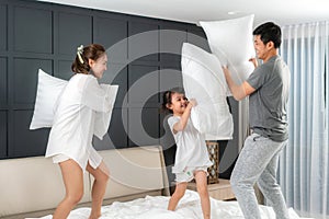 Asian happy family having funny pillow fight on white bed in bedroom for free time with father, mother and daughters feeling happy