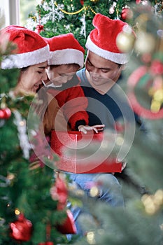 Asian happy family and little girl open magic gift box with Christmas tree in living room that decorated for Christmas festival.