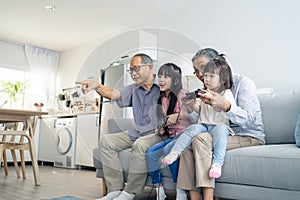 Asian happy family stay home grandparent play game with little girl. Loving senior elder older couple play video games in front of