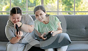 Asian happy funny lovely mother and young chubby down syndrome autistic autism little cute daughter sitting on cozy sofa smiling