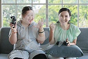 Asian happy funny lovely mother and young chubby down syndrome autistic autism little cute daughter sitting on cozy sofa smiling