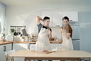 Asian happy handsome man gay couple sing and dance together in kitchen. Attractive romantic male lgbt couple wear apron, spending