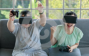 Asian happy lovely mother and young chubby down syndrome autistic autism little daughter sitting on cozy sofa wearing VR virtual