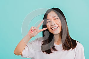Asian happy portrait beautiful cute young woman teen smile standing wear t-shirt showing finger making v-sign symbol near eye look
