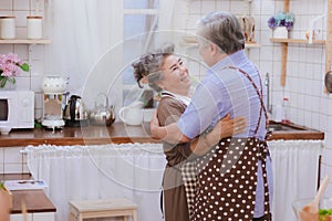 Asian happy retired senior smiling cute eldery couple hugging & holding hands together in kitchen at home Romantic relationship of