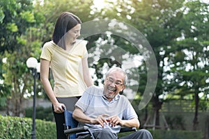 Asian happy Senior retired grandfather enjoy outdoor at green park. Attractive girl daughter pushing elderly father on wheelchair