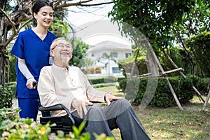 Asian happy Senior retired grandfather have fun outdoor at green park with young woman nurse. Caregiver doctor pushing elderly pat