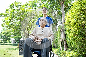 Asian happy Senior retired grandfather have fun outdoor at green park with young woman nurse. Caregiver doctor pushing elderly pat