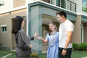 Asian happy smile young couple take keys new big house from real estate agent or realtor in front of their house after signing