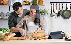 Asian happy young adult couple lover helping together for cooking in cozy home kitchen in morning, preparing meal, making salad,