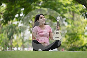 Asian healthy pregnant woman enjoying and relaxing by playing Ukulele in the park, Music time