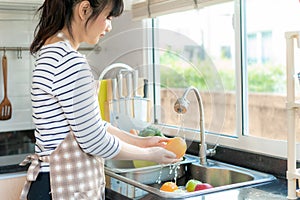 Asian healthy woman washing an orange and other fruit above kitchen sink and cleaning a fruit / vegetable with water to eliminate photo