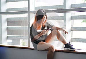 Asian highschool girl sitting by the window using smartphone