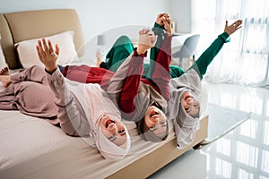 Asian hijab women and friends lay down and hands raised on the bed while having fun together