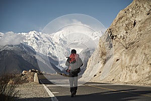 Asian hiker backpacker walking on highway with snow mountain in background