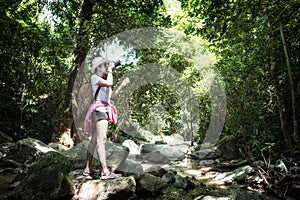 Asian hipster tourism women take a photo of waterfall in deep forest.