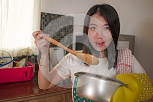 Asian home cook girl lifestyle portrait . Young happy and beautiful Korean woman in kitchen apron and glove holding cooking pot