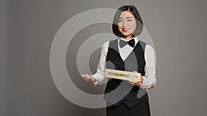 Asian hotel concierge holding restaurant sign to indicate direction