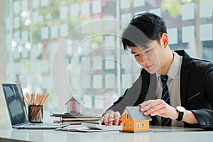 Asian house sales representative explaining details of housing contract in project to client with laptop, contract documents on ta