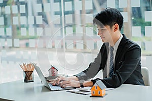 Asian house sales representative explaining details of housing contract in project to client with laptop, contract documents on ta