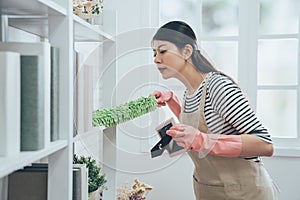 Asian housekeeper in apron dusting the bookshelf