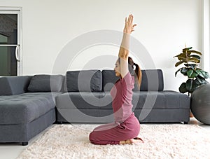 Asian housewife doing the diamond pose exercise during home workout. Female practicing yoga in Vajrasana Pose on carpet in living