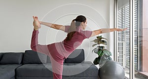 Asian housewife doing Natarajasana Pose exercise during home workout. Female practicing yoga in Lord of the Dance Pose in living