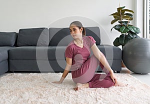 Asian housewife doing Sitting Half Spinal Twist Pose exercise during home workout. Female practicing yoga in Ardha Matsyendrasana