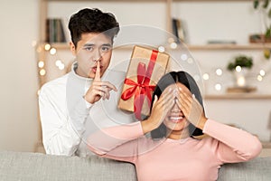 Asian Husband Holding Wrapped Gift Making Surprise For Wife Indoor