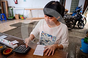 Asian Indonesian women, the owner of small local family-owned business store, or locally called warung, calculating profit by her photo