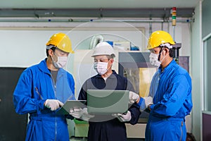Asian industrial engineers and worker in hard hats discuss product line in laptop and make showing gestures and work in a heavy