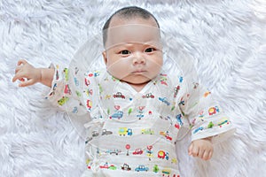 Asian Infant baby is ralaxing on the white bed. It is watching at me. It`s face is frown.