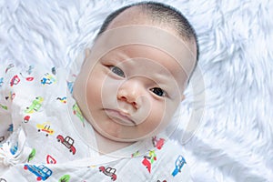 Asian Infant baby is ralaxing on the white bed. It is watching at me. It`s face is frown.