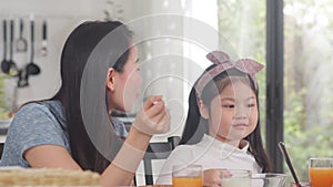 Asian Japanese family has breakfast at home. Asian mom and daughter happy talking together while eating bread, drink orange juice