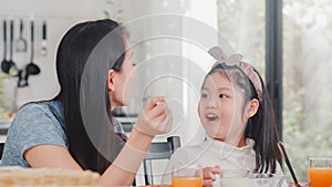Asian Japanese family has breakfast at home. Asian mom and daughter happy talking together while eating bread, drink orange juice