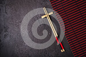 Asian Japanese table setting. Bamboo chopsticks and red black mat on black background