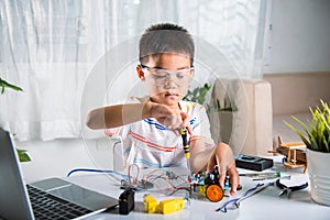 Asian kid boy assembling the Arduino robot car homework project at home photo
