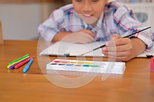 asian kid boy child schoolboy holding paint brush drawing painting watercolor. children leisure activity at home