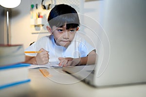 Asian Kid Boy Focused on Homework and Learning Online Alone with Laptop in Room at Home, Concentrating on Learning and Doing