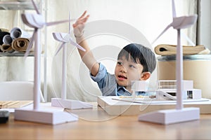 Asian kid boy playing wind turbine model in home office with home model