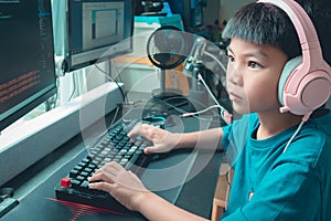 Asian kid coding and scripting program on on his game streaming desktop computer with headphone on photo