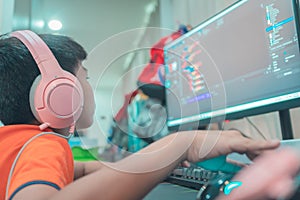Asian kid coding and scripting program on on his game streaming desktop computer with headphone on